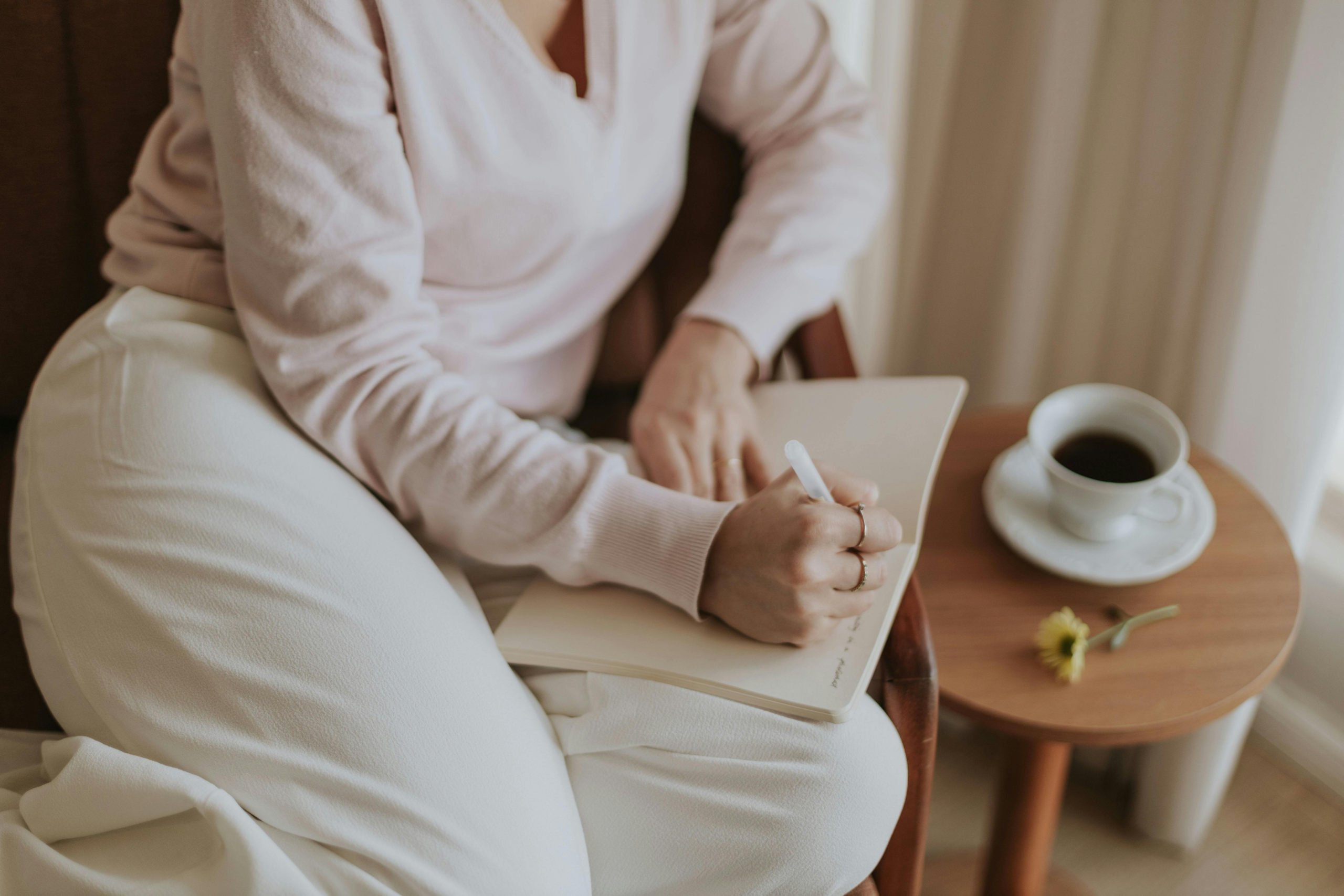 woman writing on a journal sitting on a couch next to a coffee table with a cup of coffee featuring the morning routines