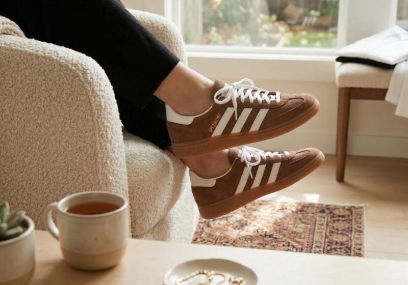 A person wearing brown and white sneakers resting their feet on a cream-colored textured chair, next to a wooden coffee table with a white mug and jewelry dish, part of a Mindful Capsule Wardrobe for a Simple Spring.